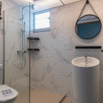 Modern bathroom featuring white marble-patterned tiles, a round pedestal basin, and a glass-enclosed shower area