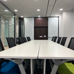 Open office with long white desks, black chairs and glass partitions