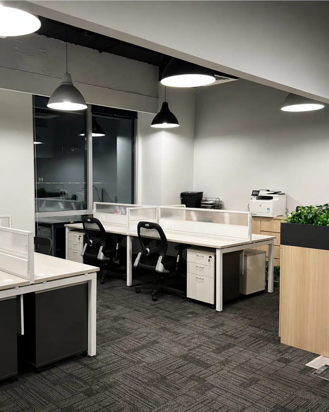 Modern open-plan office fit-out with white workstations, black chairs and planter dividers